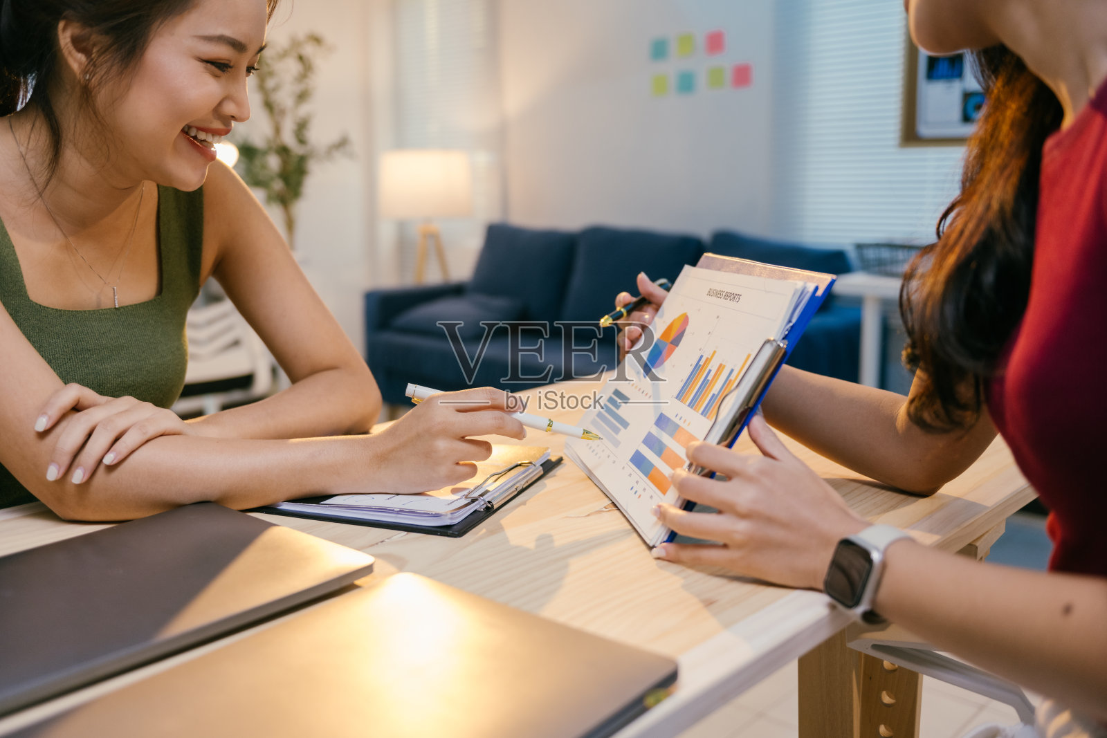 两位年轻女商人在现代办公室环境中坐在桌子旁，分析夹板上的图表和数据，讨论数据并合作进行项目。照片摄影图片