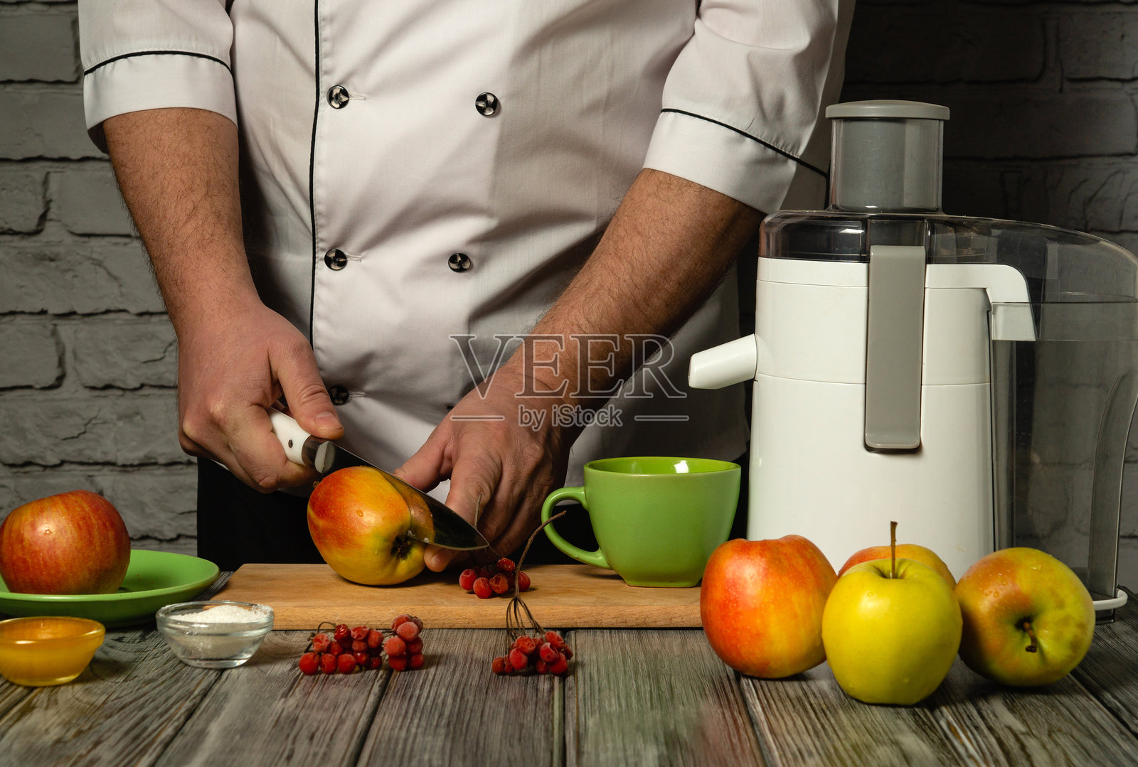 经验丰富的厨师穿着白色制服，正在用电动榨汁机切割红苹果。为午餐在餐厅或酒店厨房制作美味健康的鲜榨苹果饮品。水果饮食。照片摄影图片