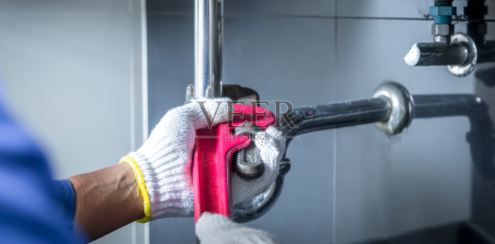 水管工的手握着扳手，正在小心地修理浴室水槽和堵塞的管道。照片摄影图片