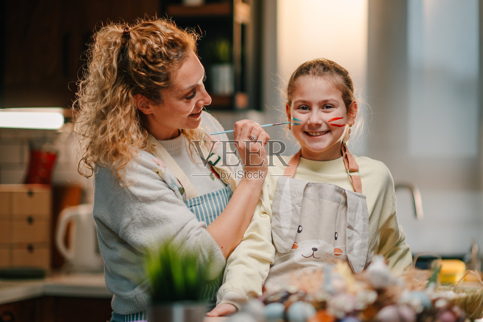 母亲在厨房为女儿画脸，同时装饰复活节彩蛋照片摄影图片
