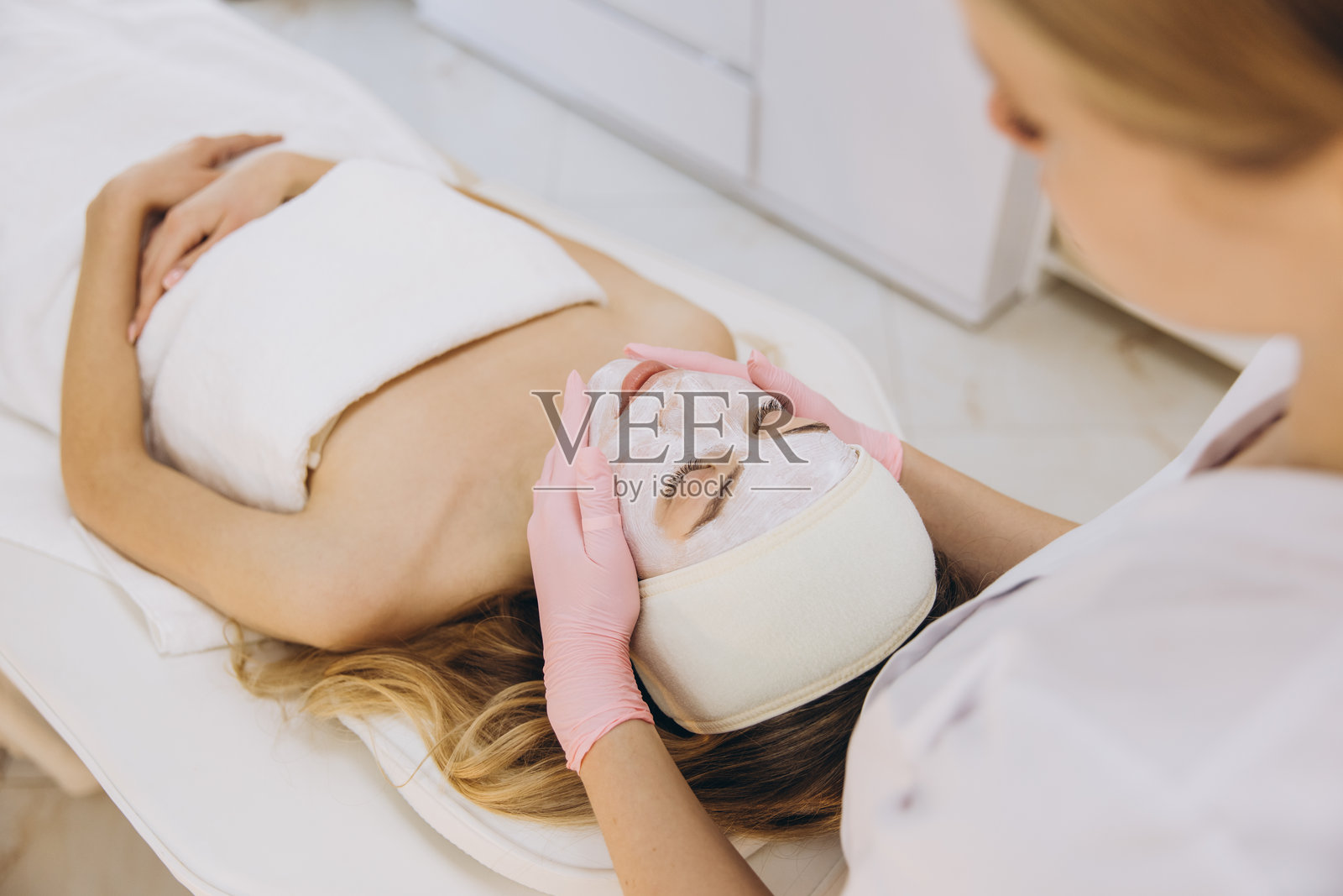 专业美容师为客户涂抹面膜，客户在治疗床上休息，突出现代水疗环境中的护肤治疗和放松。照片摄影图片