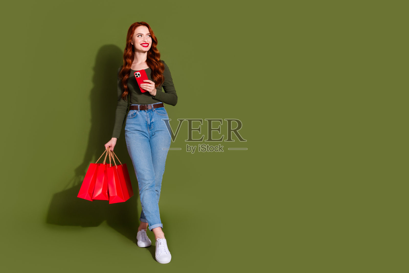 全身照，光鲜迷人的女士穿着衬衫，手持打折商品，正在打字，背景为空白的绿色。照片摄影图片