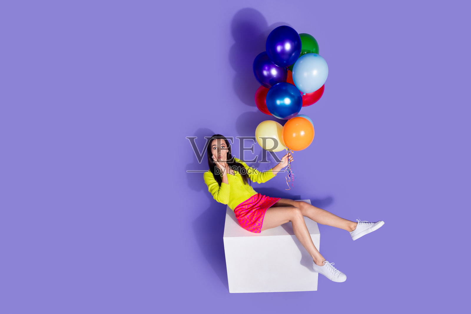 兴奋而印象深刻的可爱女孩穿着时尚衣服，手持氦气球，背景为空白的紫色。照片摄影图片