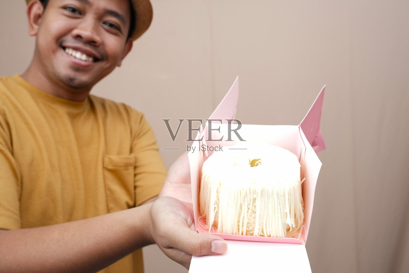 微笑的亚洲男子双手呈现一块奶酪覆盖的海绵蛋糕。照片摄影图片