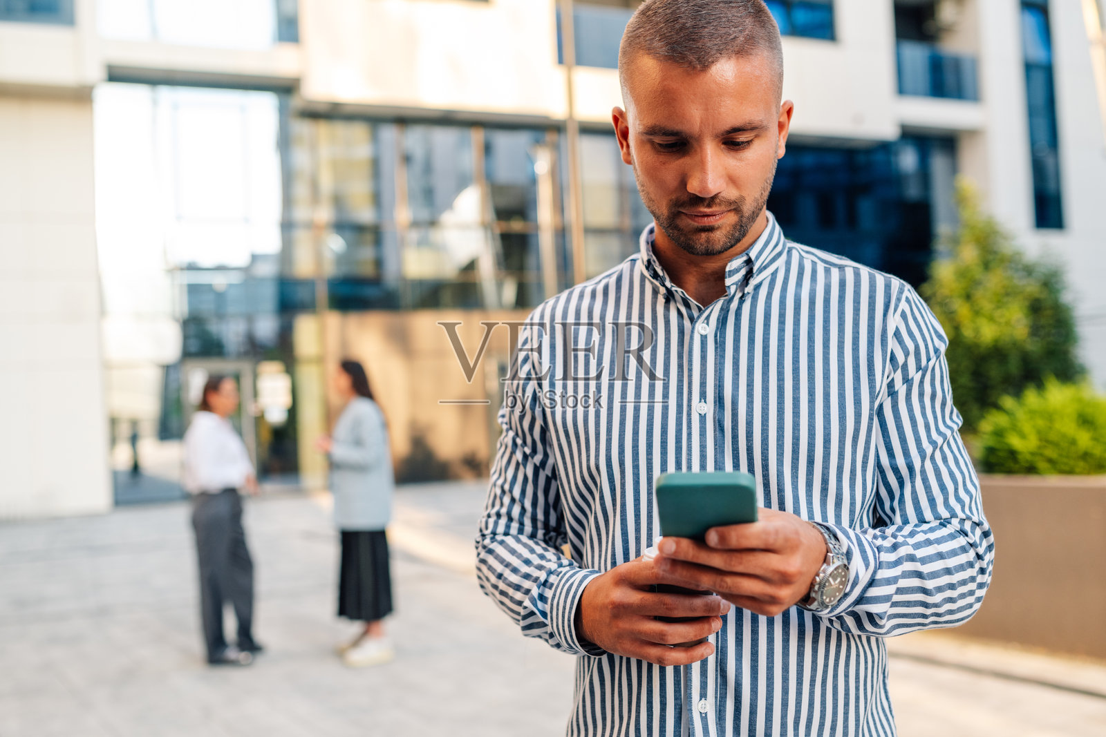 商人在办公楼外使用智能手机应用程序照片摄影图片