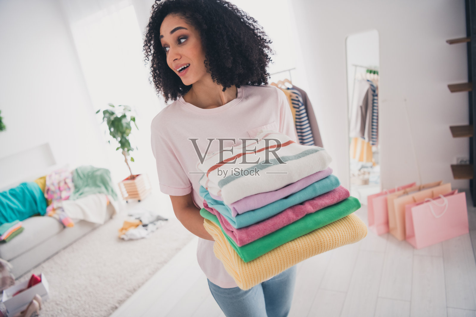 可爱的迷人女孩在室内公寓中手持时尚服装系列。照片摄影图片