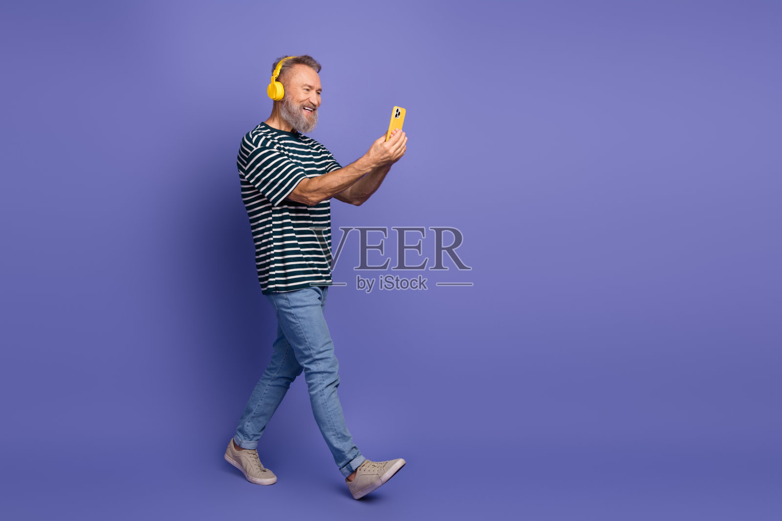 微笑的老年男子，灰色胡须，指向一旁，背景为鲜艳的紫色，穿着条纹衬衫，表情自然。照片摄影图片