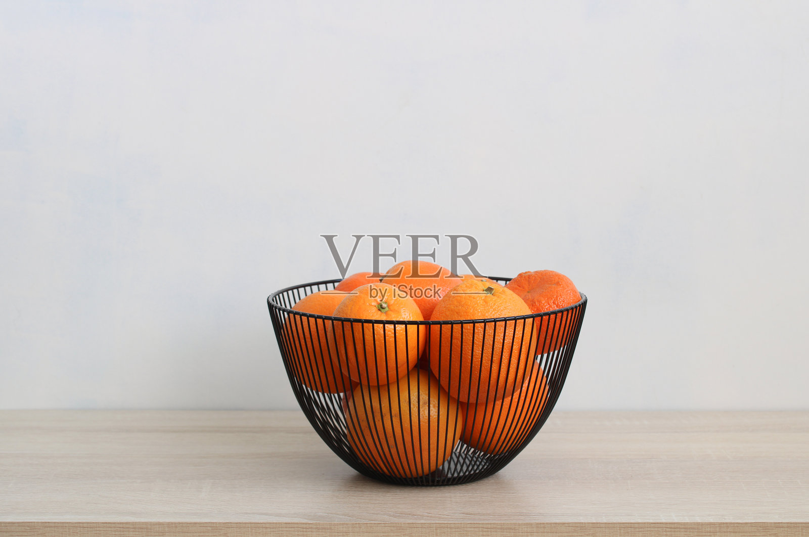 新鲜的橙子静静地放在现代金属篮子里，摆放在木桌上照片摄影图片