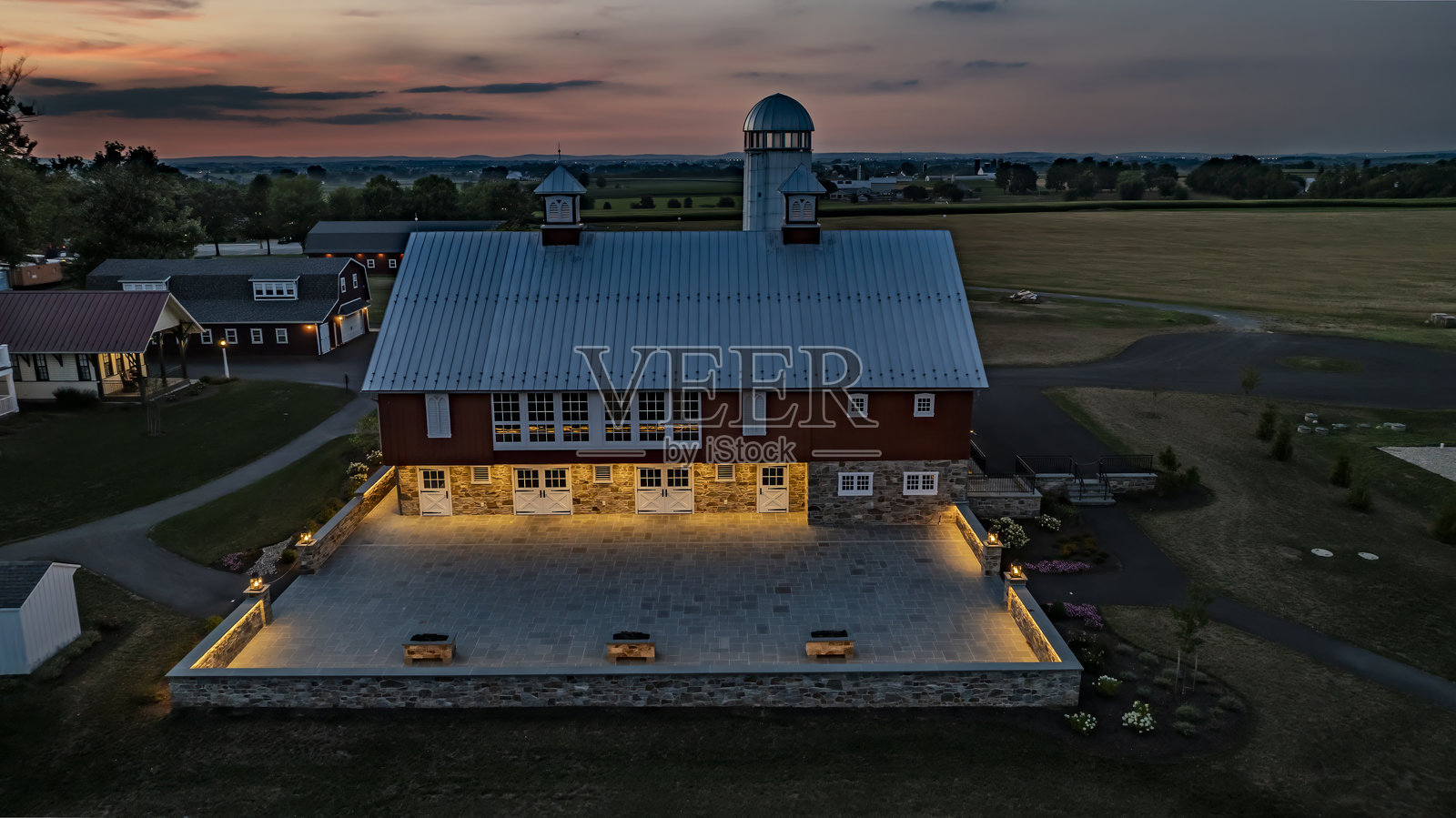黄昏时分的农场，红色谷仓、筒仓和灯光照亮的庭院照片摄影图片