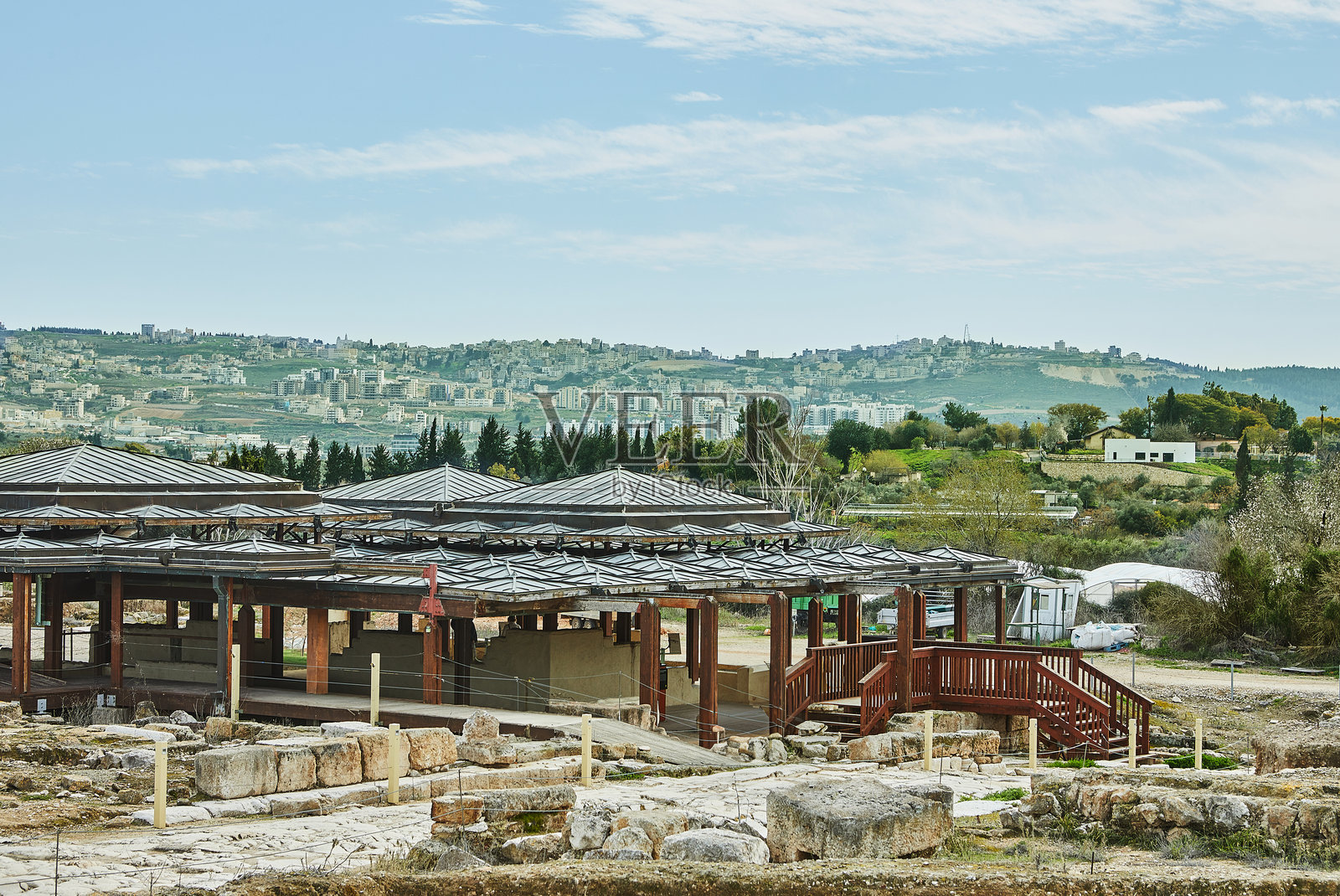 一个有保护结构的考古遗址，展示着历史遗迹和古代文明的遗物，背景是一座现代城市。照片摄影图片