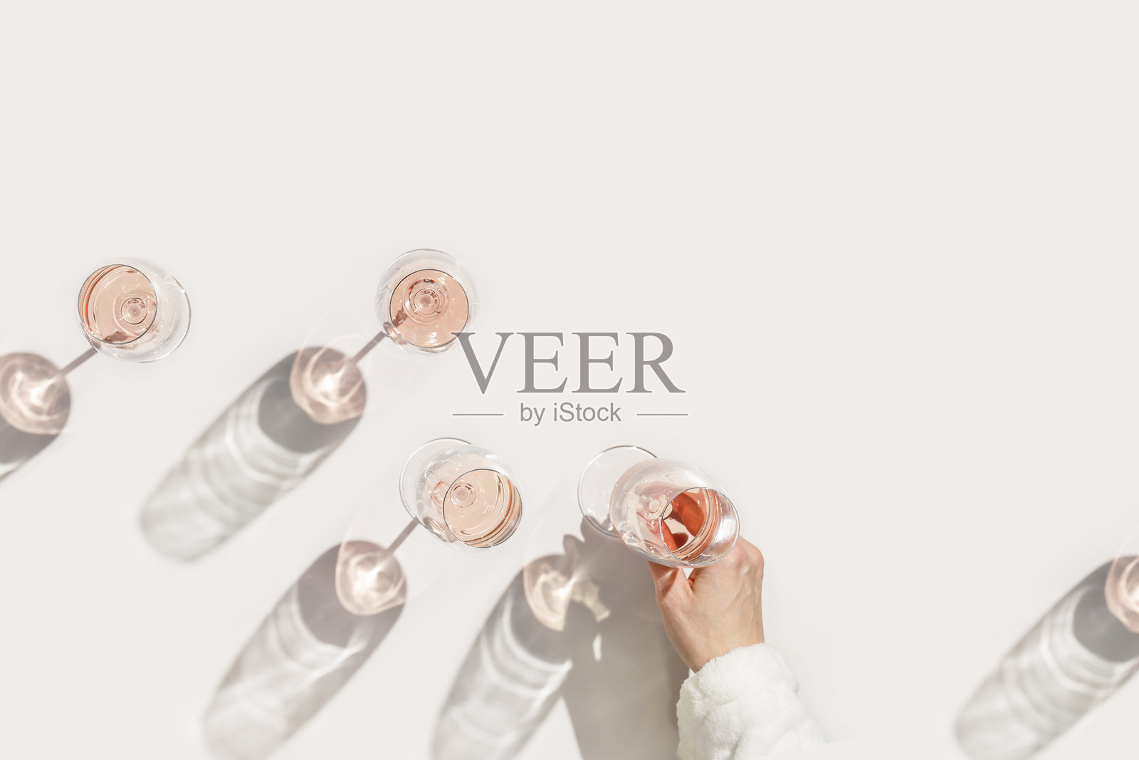 在酒会中摆放的玫瑰红酒杯，极简概念。女性手中拿着的水晶酒杯俯视图，阳光照射下的阴影和眩光，米色和粉色背景，酒精饮品，留白空间。照片摄影图片