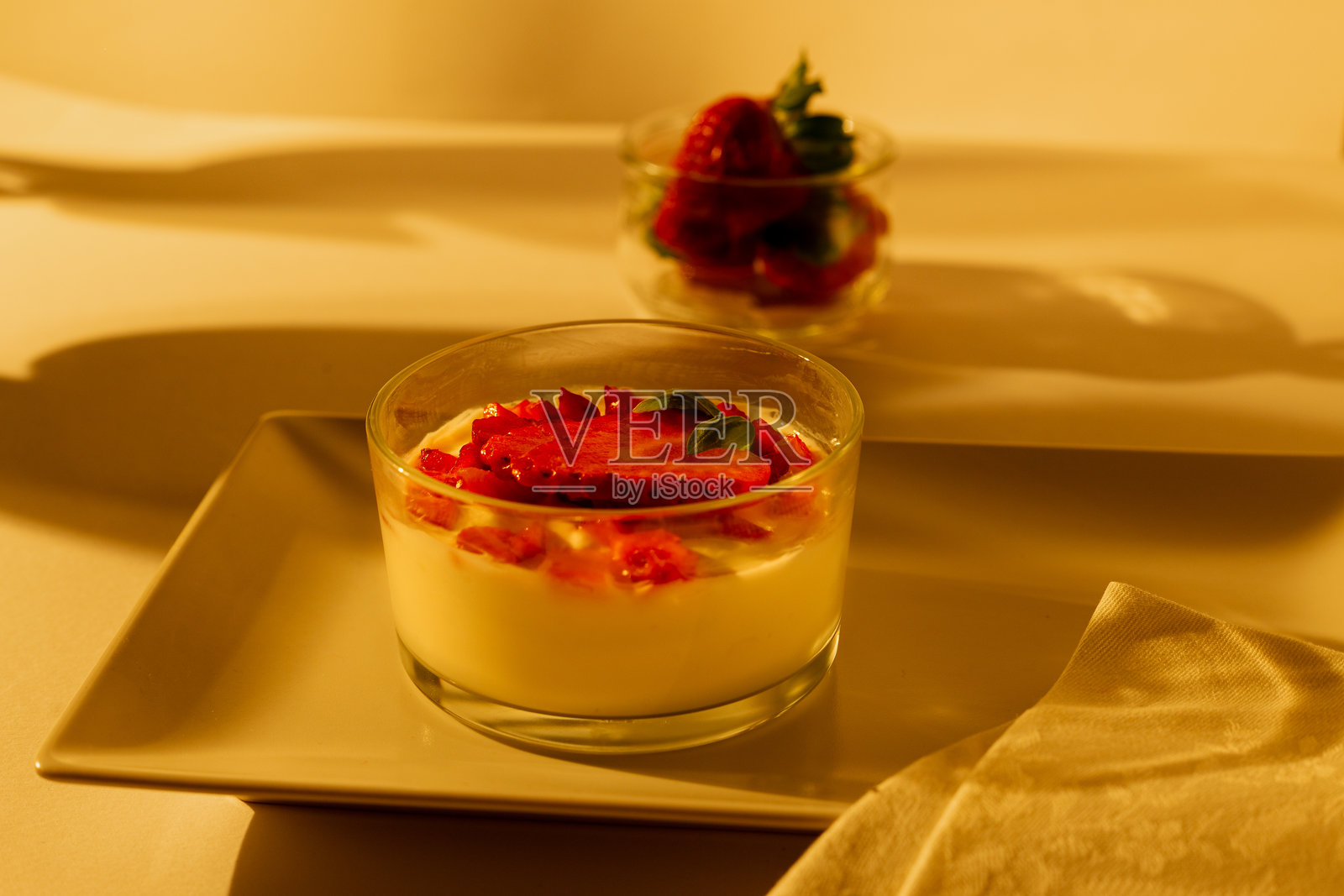 日落时分，白色盘子上的希腊酸奶和草莓，伴有植物的阴影。照片摄影图片