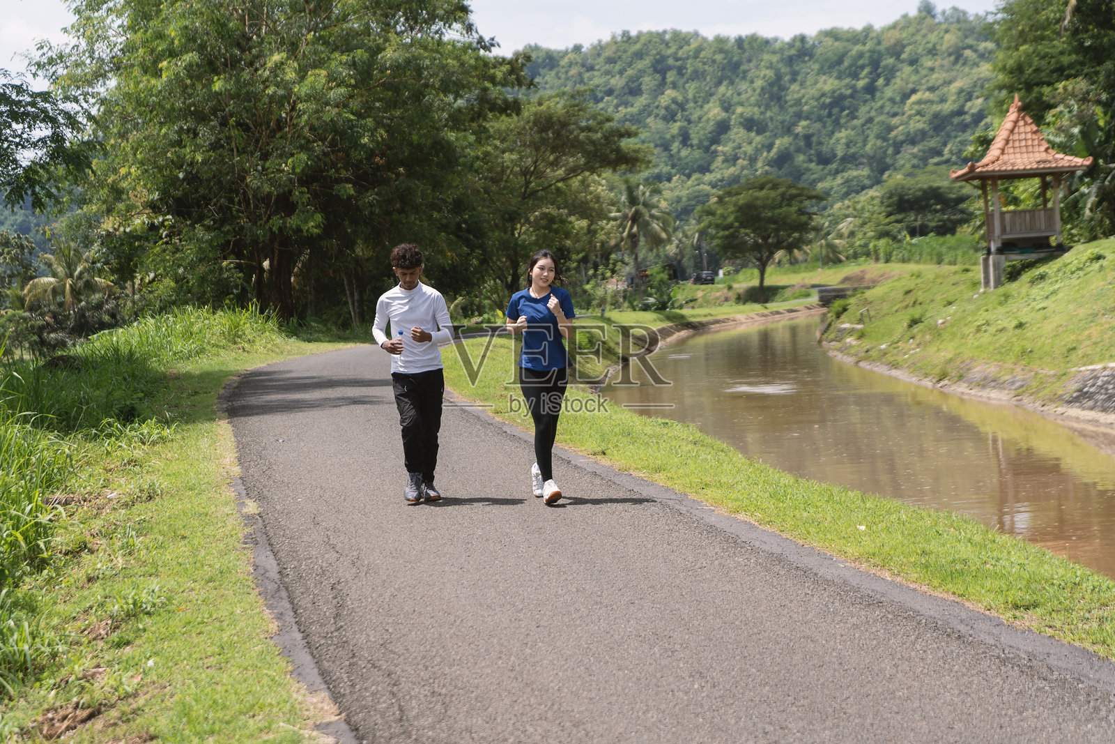 活力四射的亚洲年轻情侣在乡村地区慢跑，手中拿着水瓶照片摄影图片