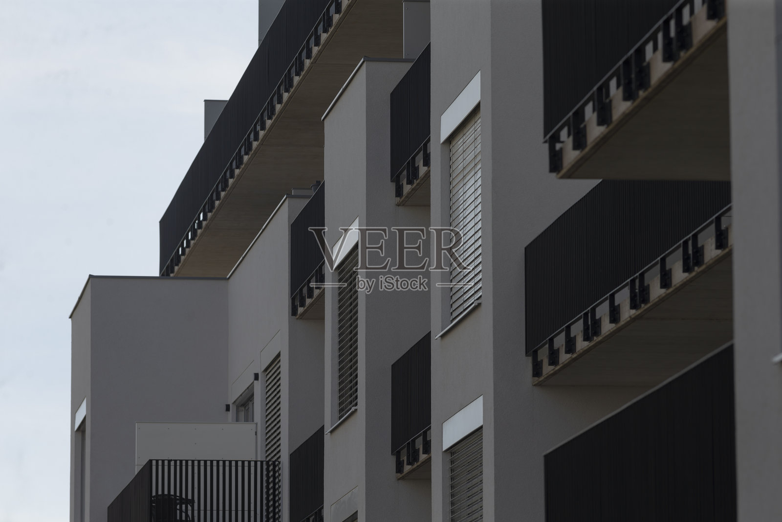 一栋高楼，拥有众多窗户和阳台，背景是阴 cloudy 的天空。照片摄影图片