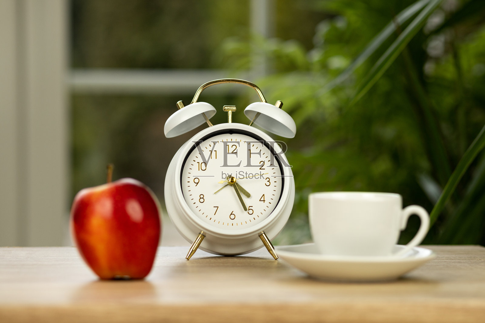桌子上有一个红苹果、一杯咖啡和一个闹钟。餐饮计划照片摄影图片