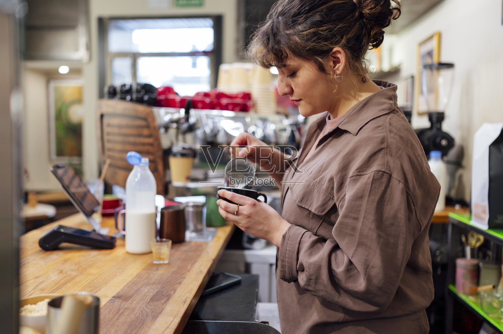 咖啡师在时尚咖啡店的吧台上为卡布奇诺倒牛奶入咖啡杯中照片摄影图片