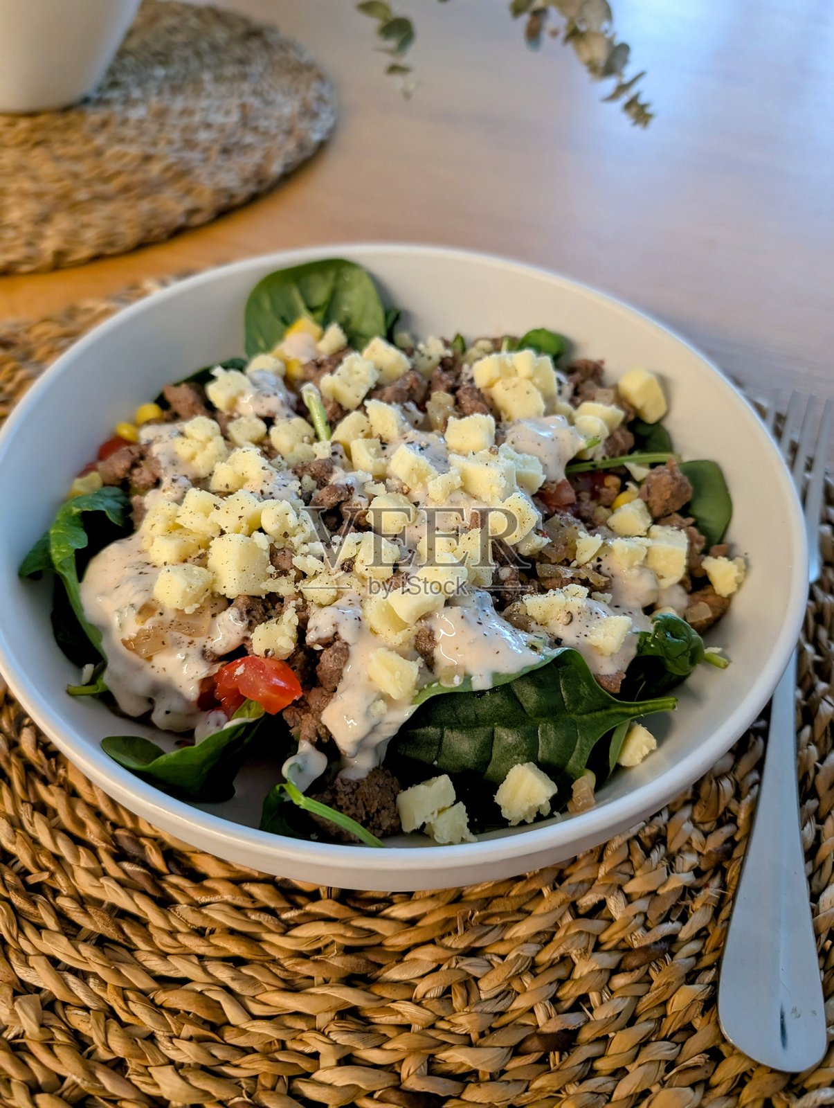 自制汉堡沙拉放在白色碗中，置于编织餐垫上照片摄影图片