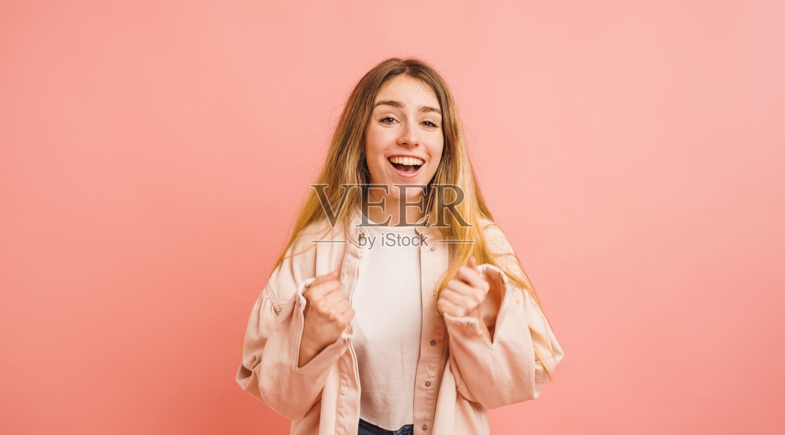 兴奋的年轻女性在粉色背景上庆祝成功照片摄影图片
