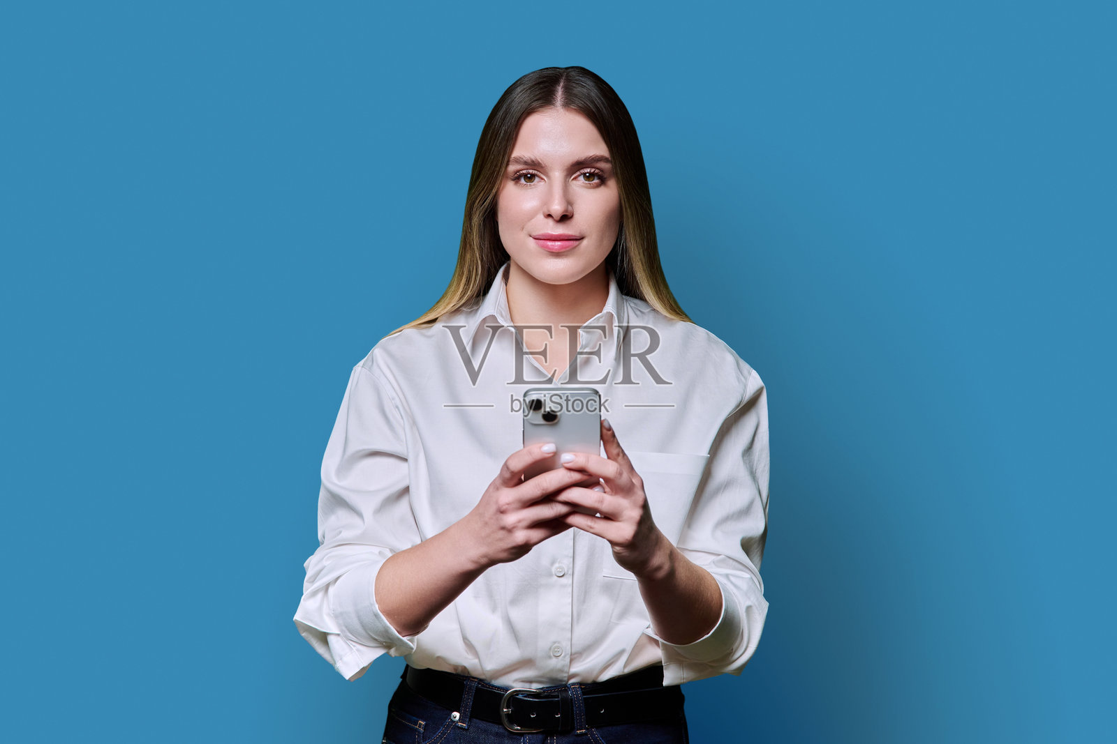 年轻漂亮的女性手持手机，面向蓝色背景的摄像机。照片摄影图片