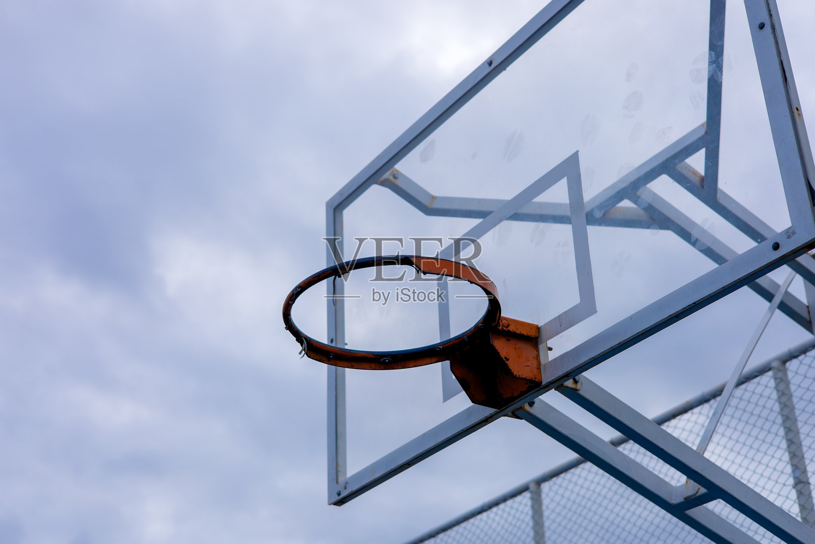户外篮球场上，篮球架与多云的天空在傍晚时分相映成趣照片摄影图片