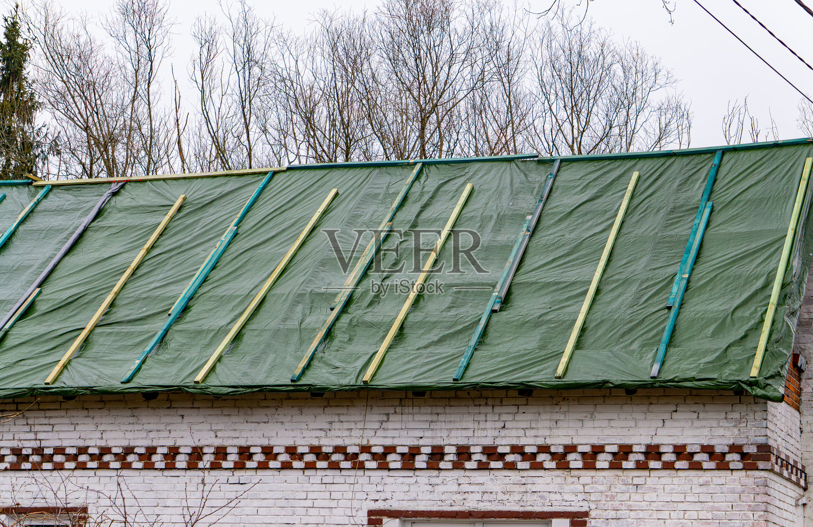 乡村老砖房的屋顶修理。屋顶覆盖着塑料膜以防止洪水。乡村建筑。照片摄影图片