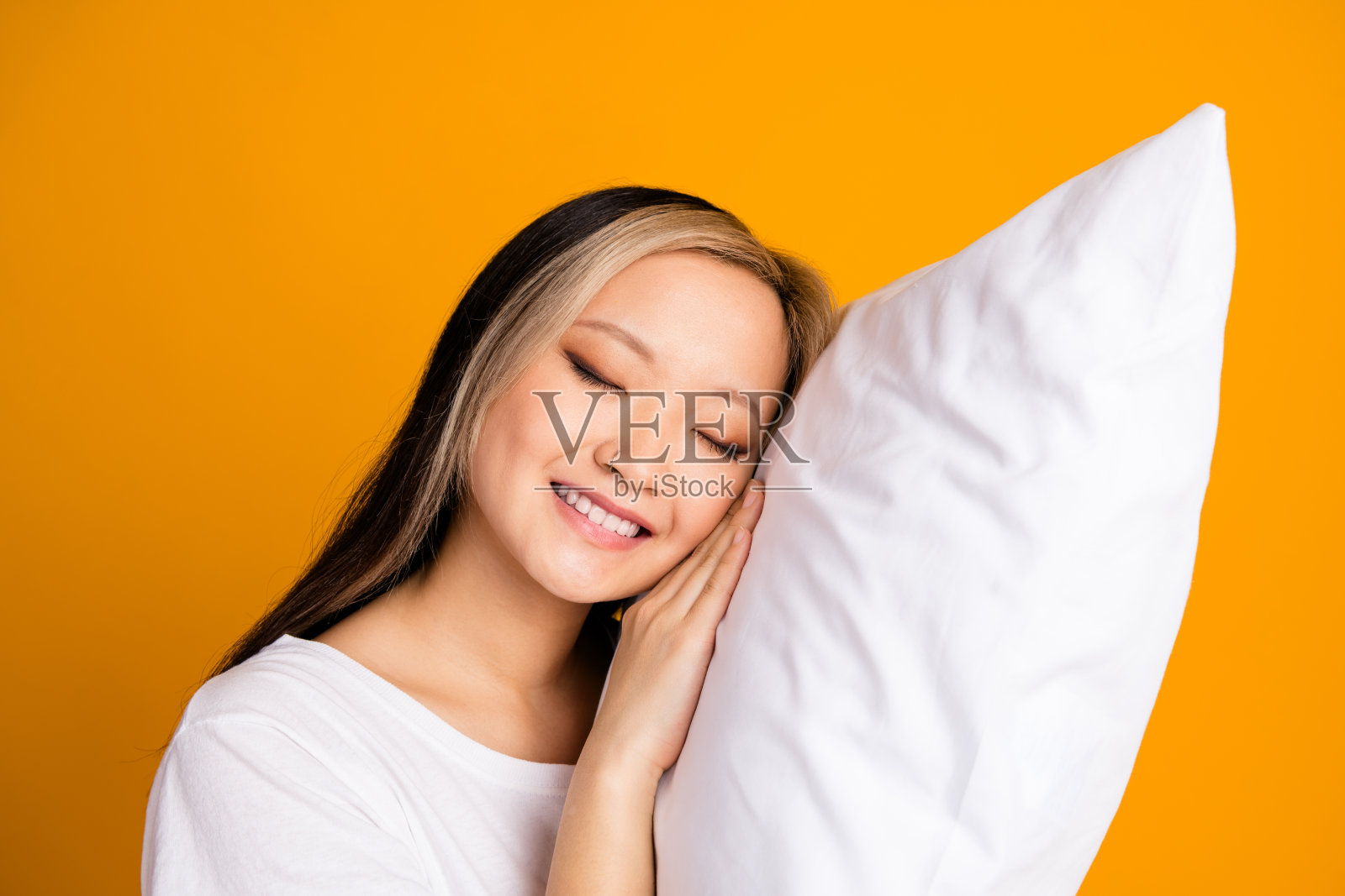 可爱迷人的梦幻女性穿着白色时尚睡衣，柔软的枕头，背景为黄色。照片摄影图片