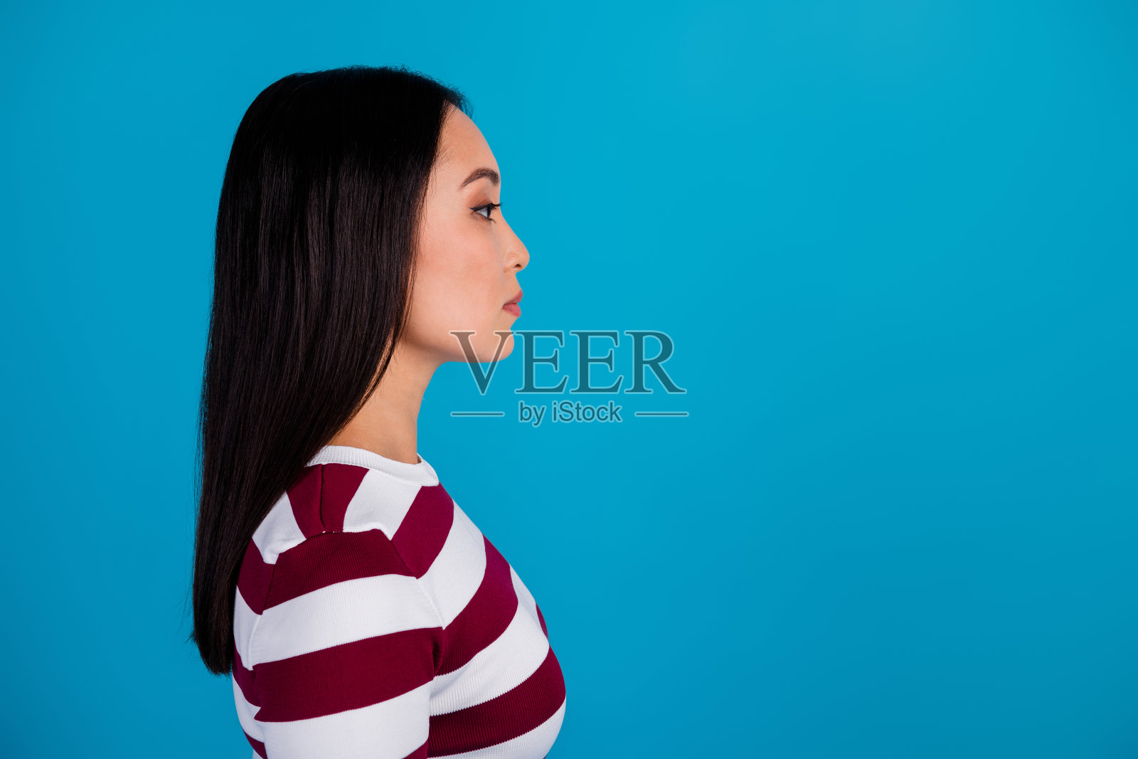 年轻女性侧面肖像，长棕色头发，穿着条纹衬衫，背景为鲜艳的蓝色。照片摄影图片