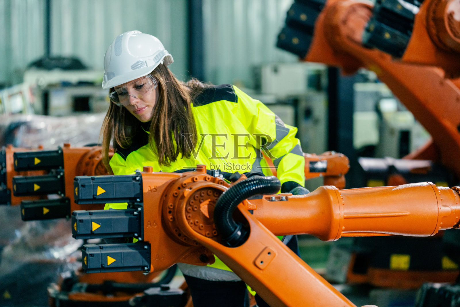穿着安全装备的女性在工业环境中操作机器人手臂照片摄影图片