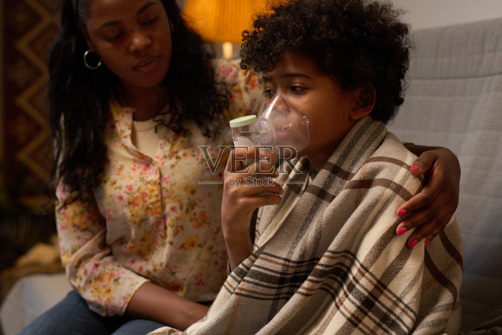 母亲陪伴下，坐在沙发上使用吸入器的安慰孩子照片摄影图片