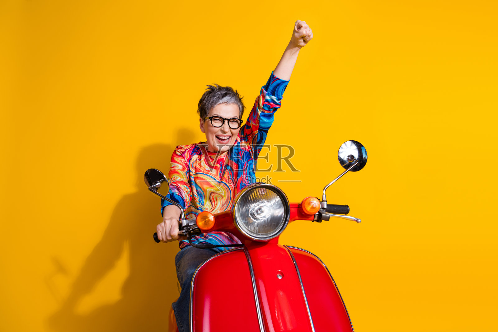 漂亮的老年女士骑自行车，举起拳头，背景为黄色。照片摄影图片