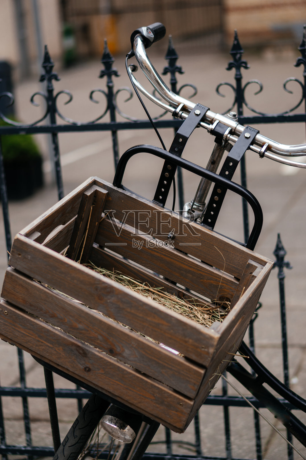 一辆复古自行车，前面装有一个装满干草的木箱，停靠在城市环境中一座华丽的铁艺围栏旁。照片摄影图片