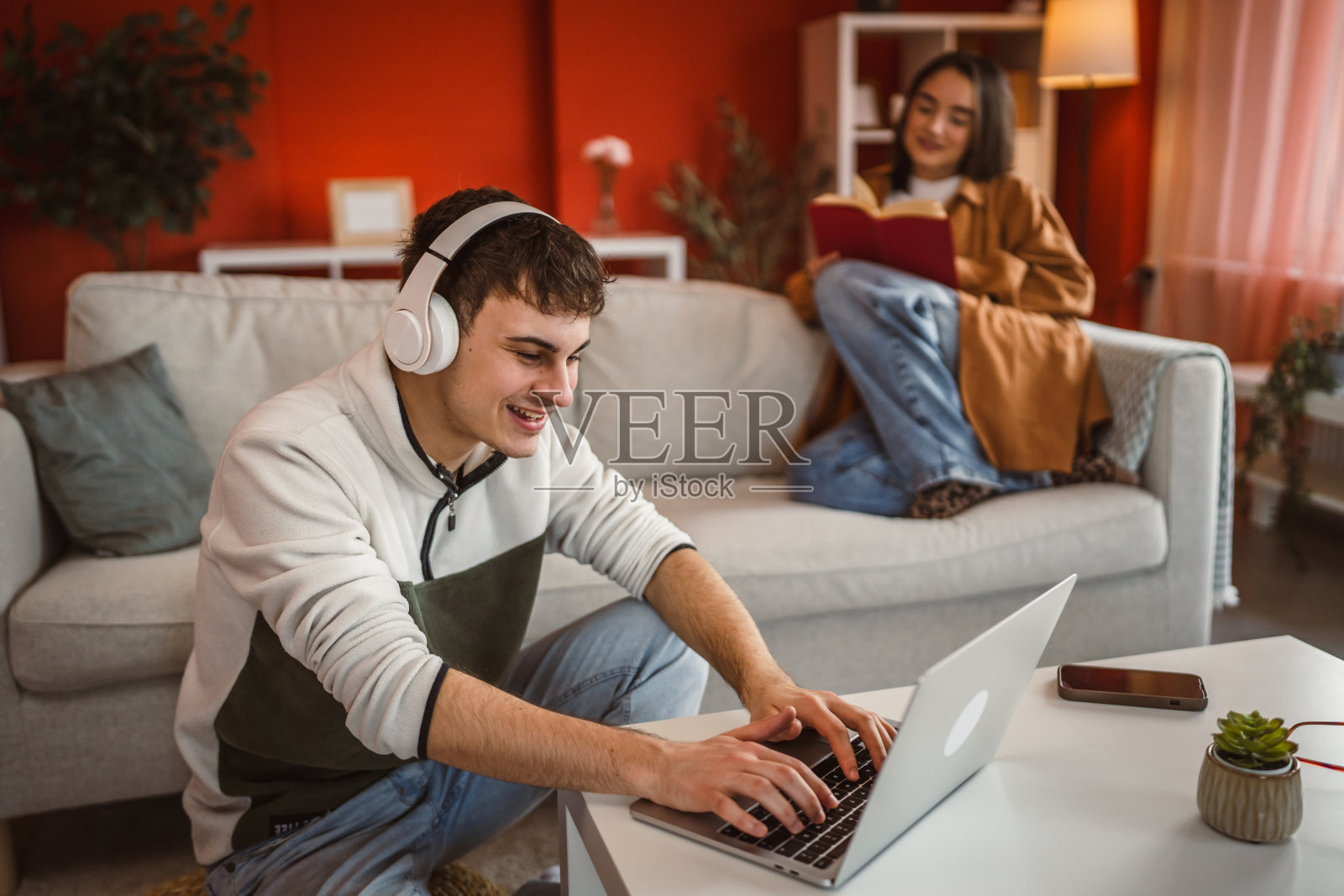 男人在家用笔记本电脑工作，女人在沙发上看书。照片摄影图片