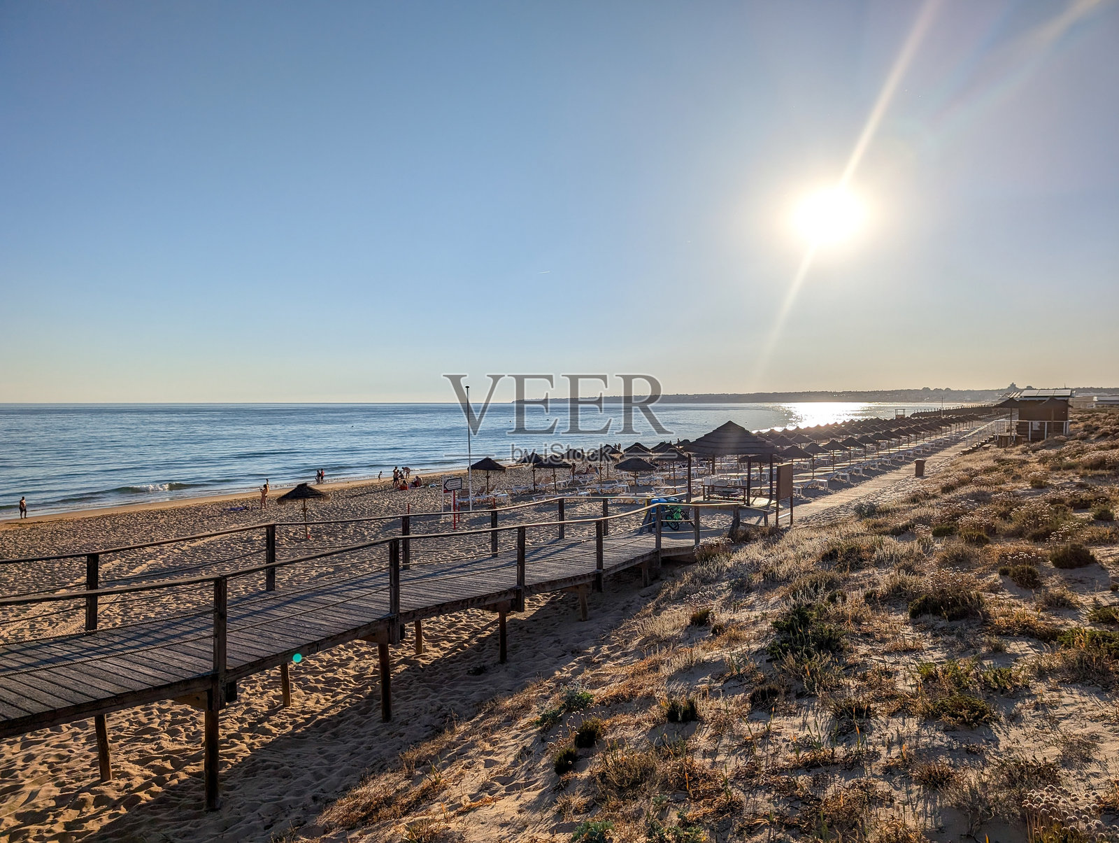 在阳光明媚的日子里，游客们沿着木栈道走向Praia da Falésia的金色悬崖，体验阿尔加维海岸的原始美景。照片摄影图片