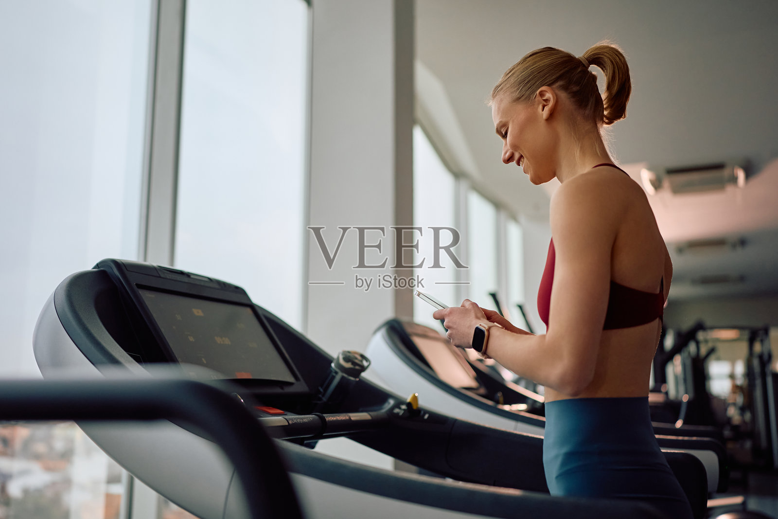 快乐的运动女性在跑步机上锻炼时使用智能手机。照片摄影图片