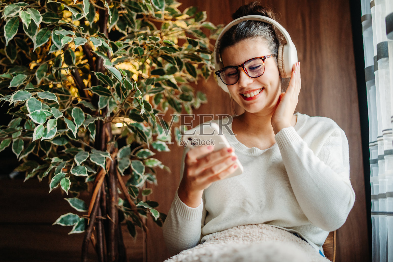 年轻的白人女性在窗边听音乐并唱歌照片摄影图片