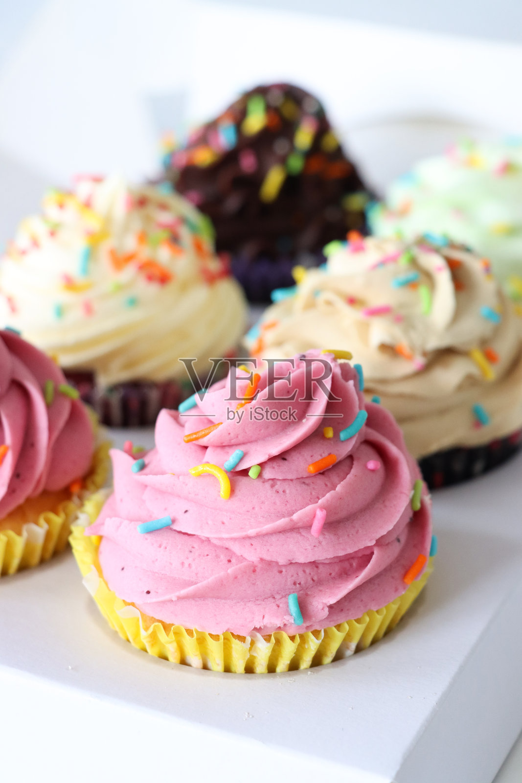 两排六个纸杯蛋糕，装饰着糖霜漩涡，放在一个面包店的纸箱中，撒上五彩糖屑，前景聚焦。照片摄影图片