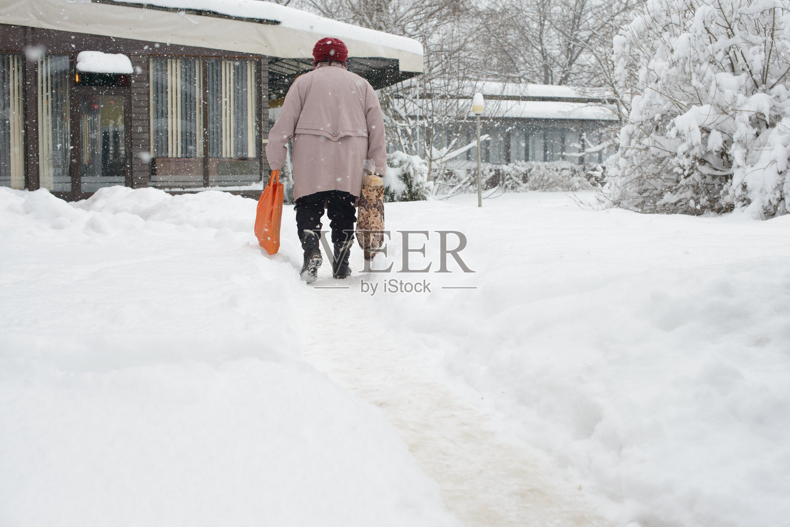 老年人提着购物袋走在雪中照片摄影图片