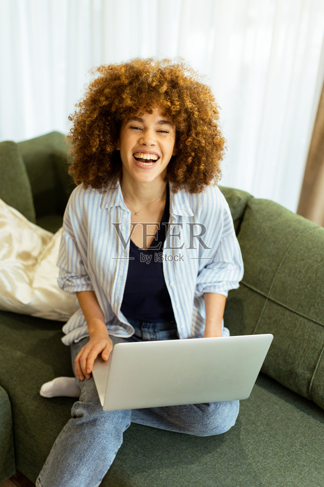 年轻女性在阳光明媚的客厅里，享受着舒适的时光，专注于她的笔记本电脑。照片摄影图片