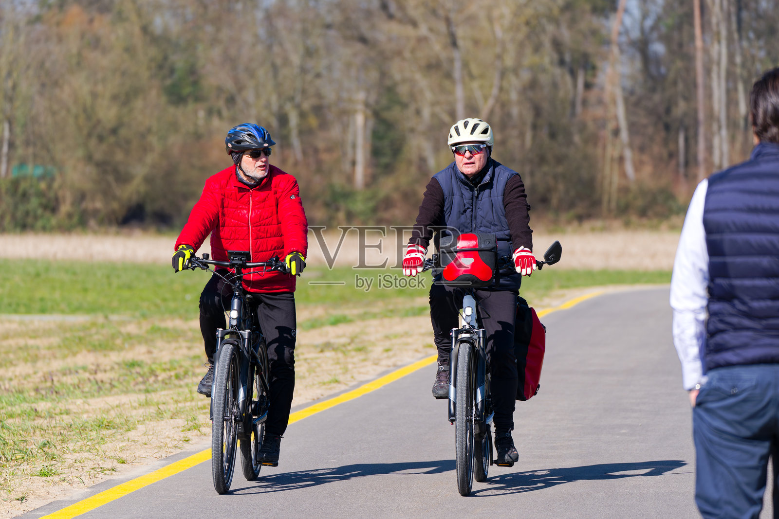两位男性老年骑自行车者在阳光明媚的晚冬日，从瑞士苏黎世克洛滕机场骑过电动自行车。照片摄影图片