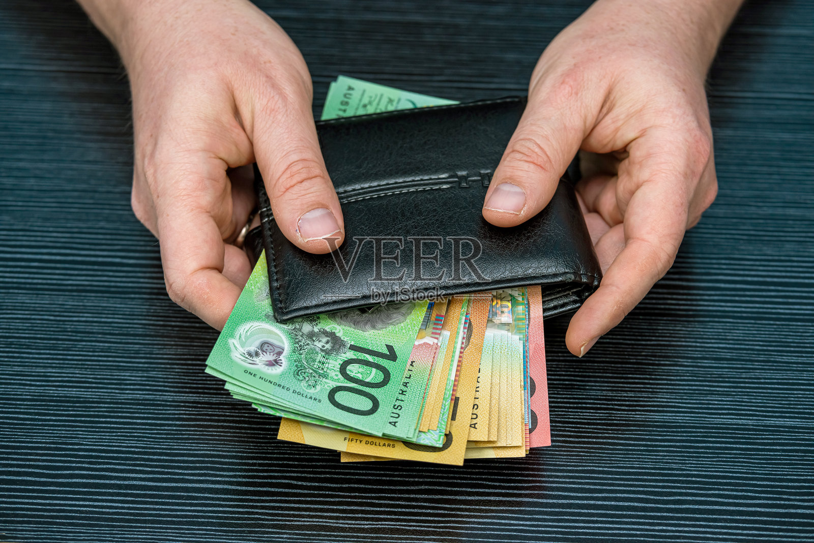 男性手从黑色皮革钱包中取出新的50和100澳元钞票。照片摄影图片