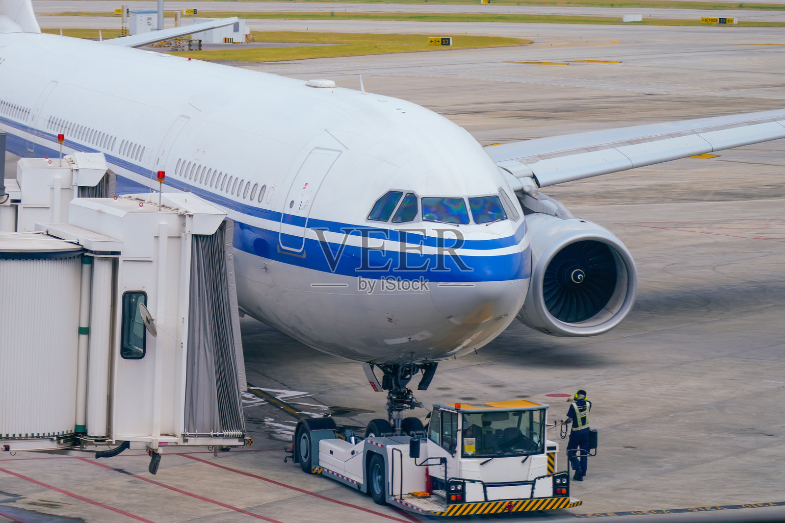 宽体客机的机头驾驶舱，飞行员在登机桥上准备起飞，身后是准备推回的机坪和拖车。照片摄影图片