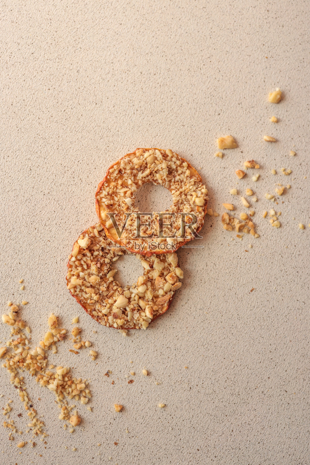 一堆干苹果片，上面撒有碎坚果。健康的自制水果脆片，搭配坚果，背景为浅色。天然有机零食，素食食品，减肥甜点，特写。照片摄影图片