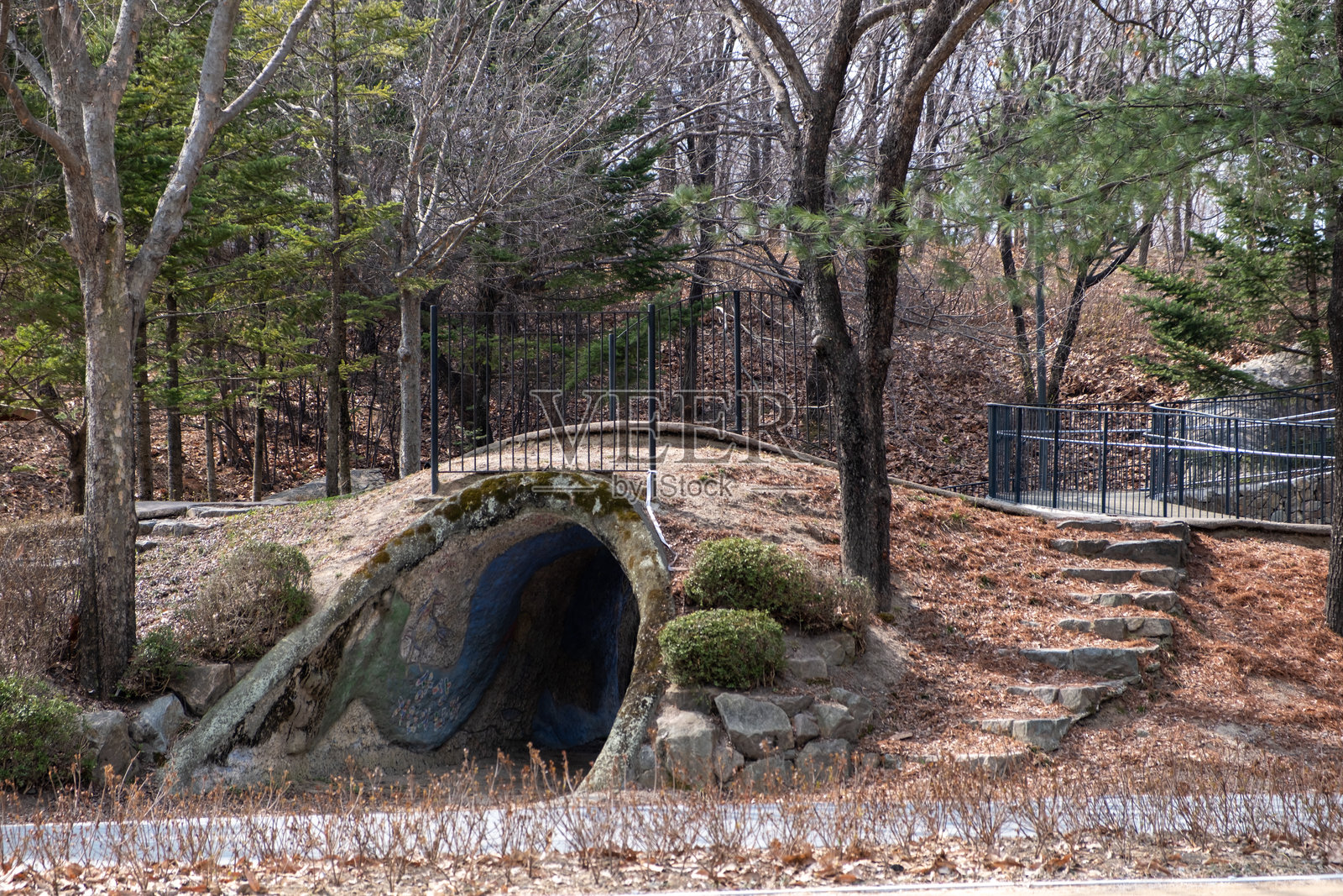 一个隧道山，像一个洞穴。周围有树木、灌木丛和通往围栏小径的石阶。在首尔森林中。照片摄影图片