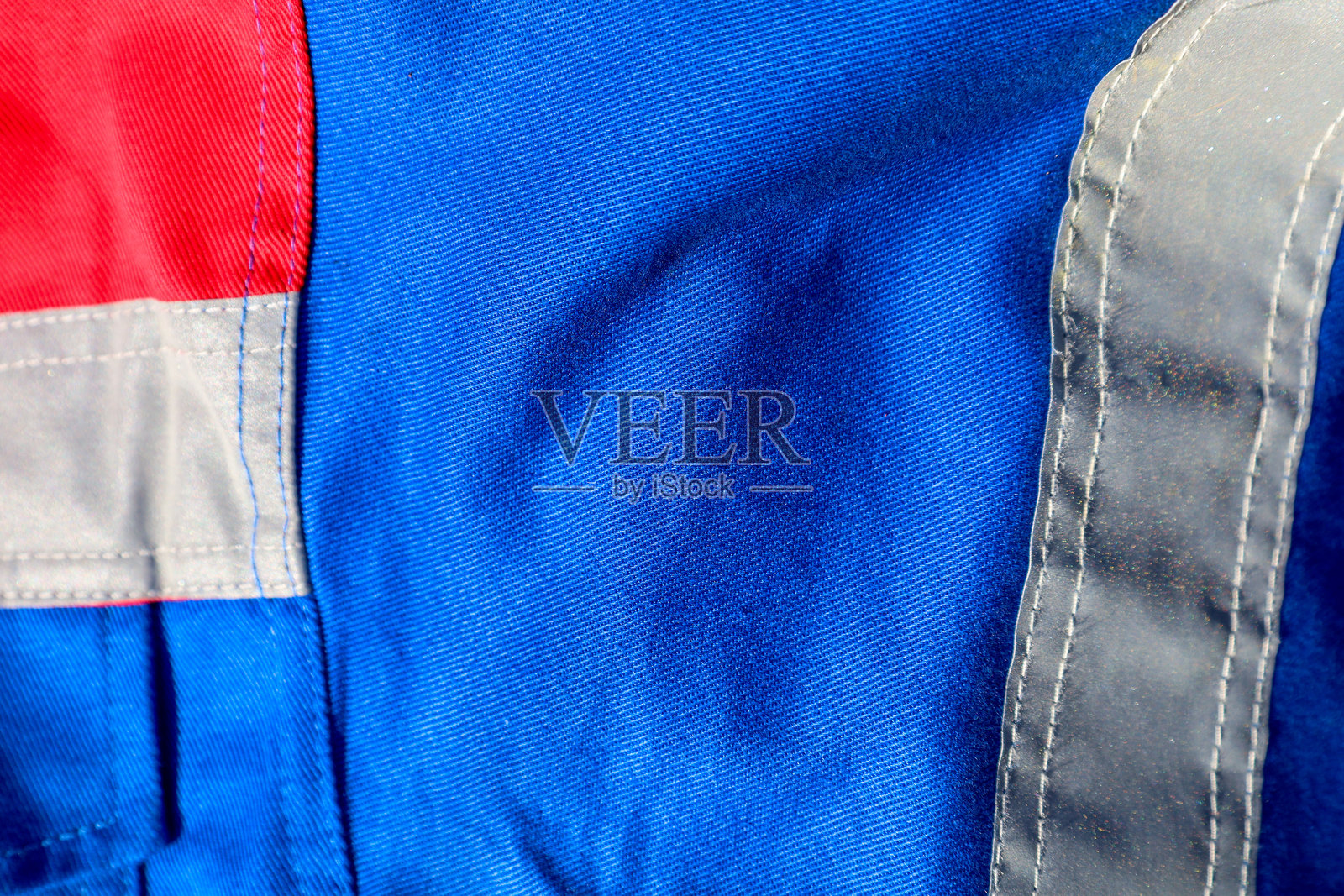 这张照片展示了一部分工作服的特写。照片中有蓝色面料，带有红色插片和灰色反光条。照片摄影图片