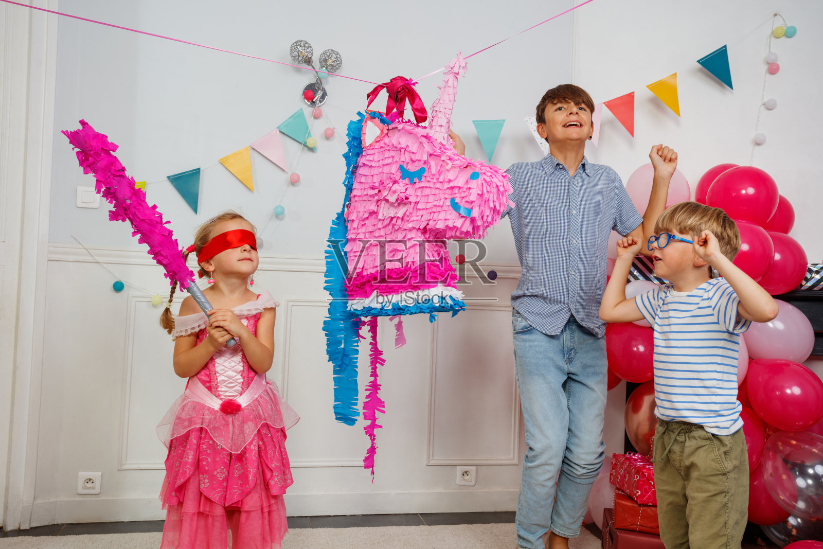 蒙着眼睛的孩子穿着裙子，正用棍子瞄准独角兽皮纳塔。照片摄影图片