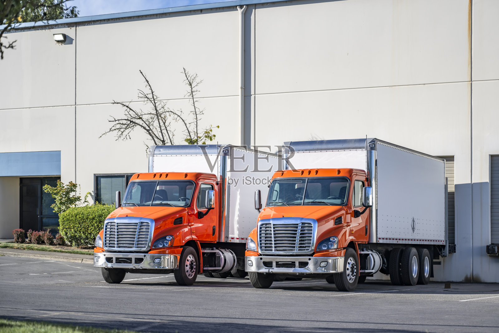 橙色中型日间驾驶室卡车与箱式拖车停在仓库装卸码头，正在装载货物以备下一个本地配送。照片摄影图片