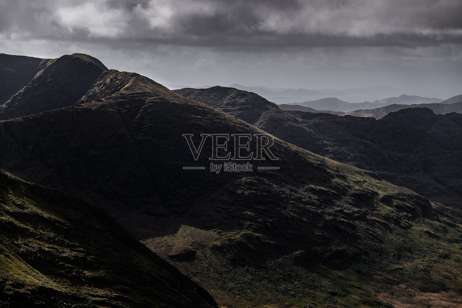 这张照片描绘了一系列山脉。最近的山脉显示出岩石、深棕色和黑色的坡度。照片摄影图片