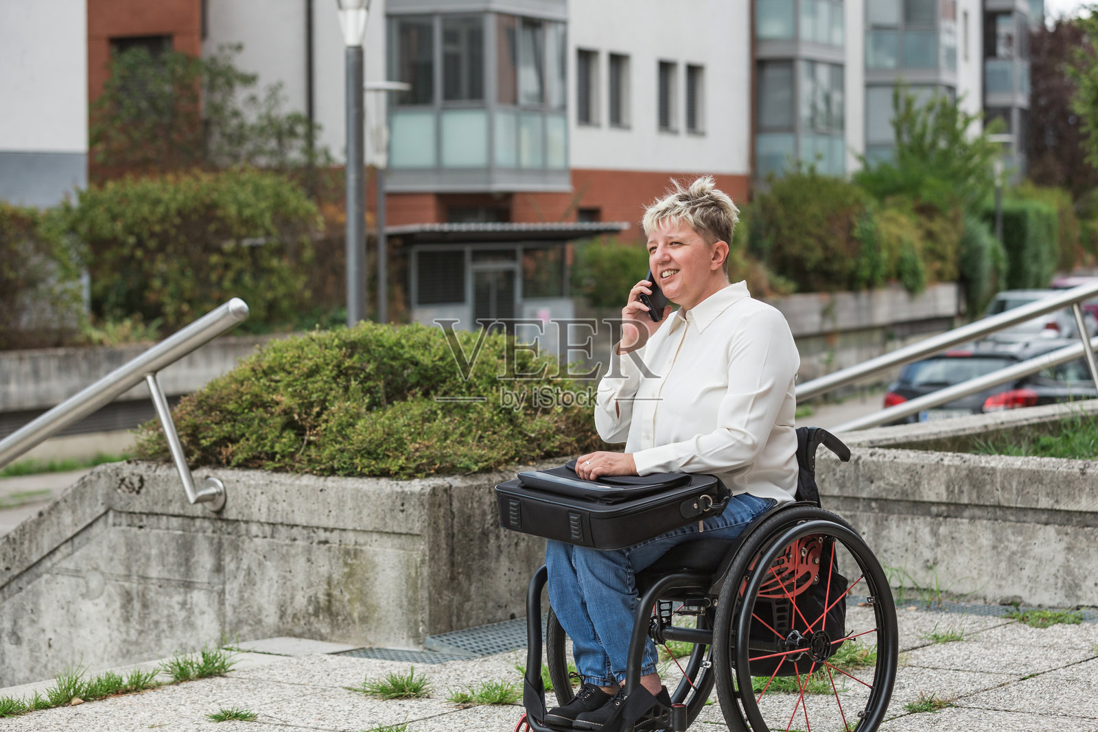 微笑的女性，坐在轮椅前面她的住宅楼照片摄影图片