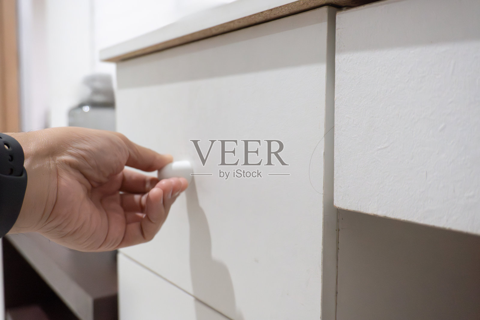 一只手伸向一个简单衣柜的白色抽屉，突显了极简家具的实用性。照片摄影图片