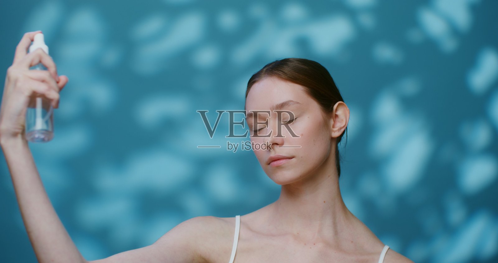 一位年轻的白人模特在脸上喷洒液体，未化妆。照片摄影图片